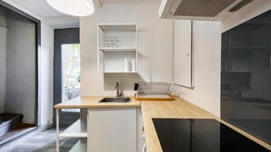 A modern kitchen with a wooden countertop, a sink, and a black stove. There are white cabinets and a window providing natural light.