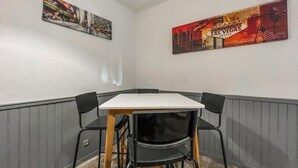 A corner dining area with a white table and black chairs. There are two wall-mounted artworks depicting urban scenes and the Las Vegas sign.
