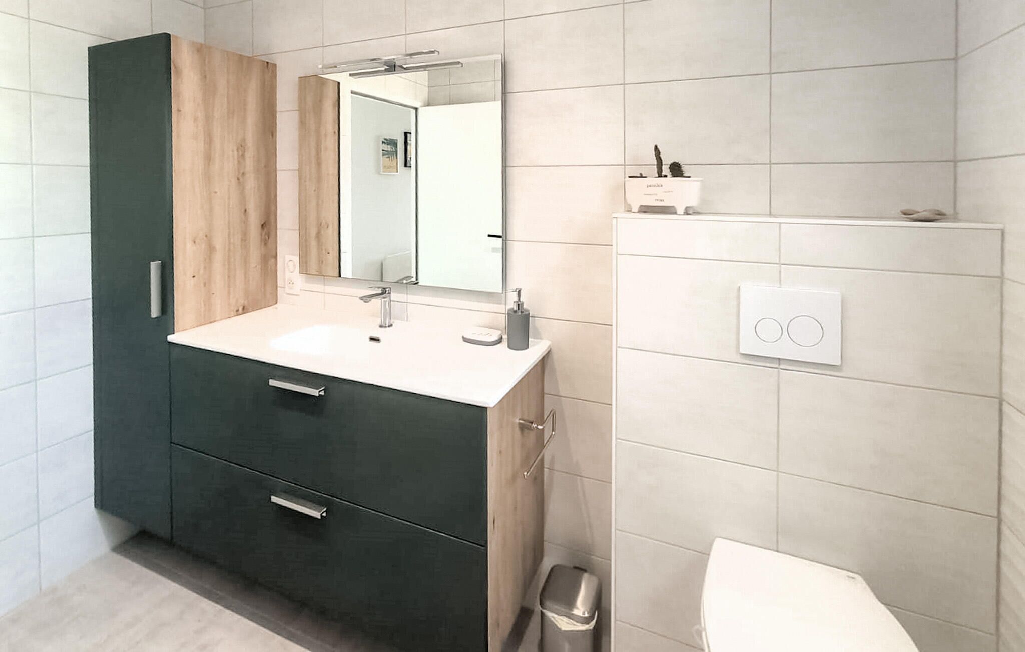 Un baño moderno con tocador verde oscuro, encimera blanca y espejo sobre el lavabo.