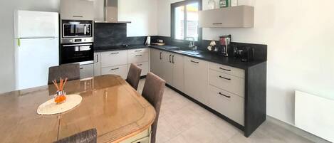 A modern kitchen with a dining area, featuring a built-in oven, microwave, and a coffee maker on the counter.