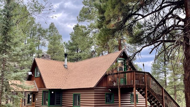 A log cabin with a steeply pitched roof, a chimney, and a wooden staircase leading to a deck. - Rustic Route 66 Homestead (Parks)