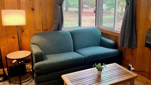 A cozy room with a green sofa, a small round table, and a window with curtains. - Rustic Route 66 Homestead (Parks)