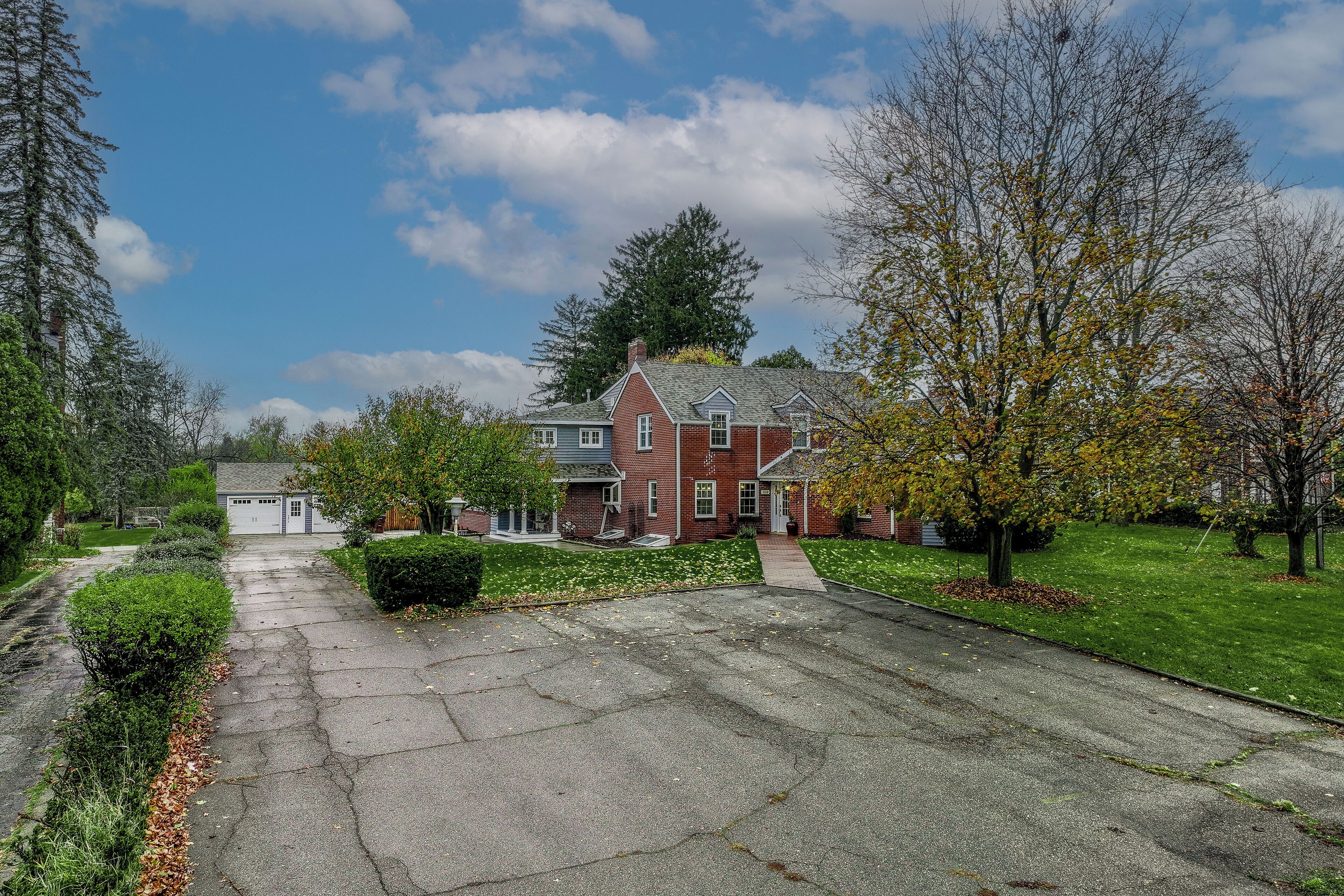 A residential street with a brick house, a driveway, and a lawn.