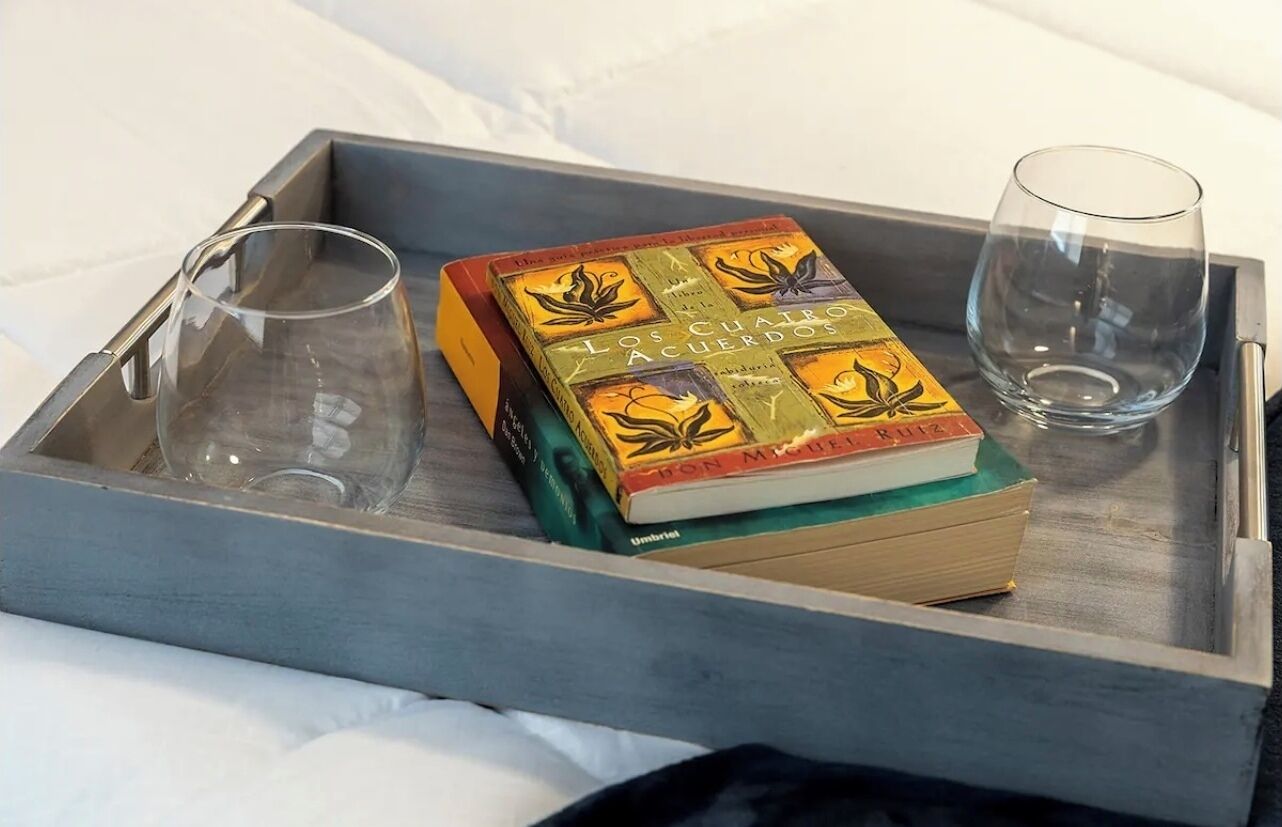 En bakke med en bog med titlen 'Los Cuatro Acuerdos' og to glas på en seng.