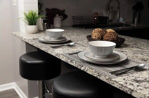 A kitchen counter with a marble backsplash, a potted plant, a cat, and a bowl of noodles. - Modern Oasis, 20 minutes from Downtown (Redford)