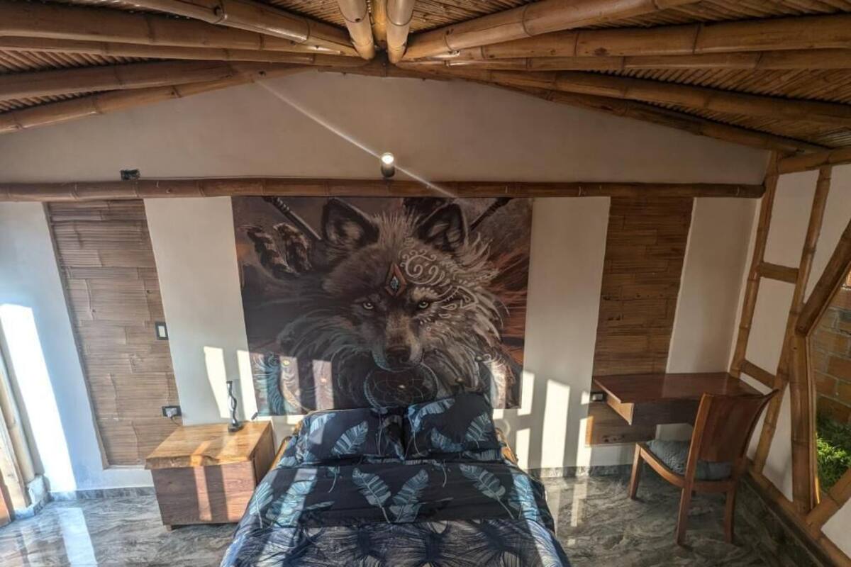 Une chambre dotée d’un lit orné d’une grande fresque représentant un loup, de poutres en bois au plafond, d’une table de chevet en bois et d’une table à manger avec des chaises.