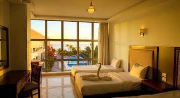 Habitación de hotel con dos camas, un escritorio y vistas a una piscina y palmeras.