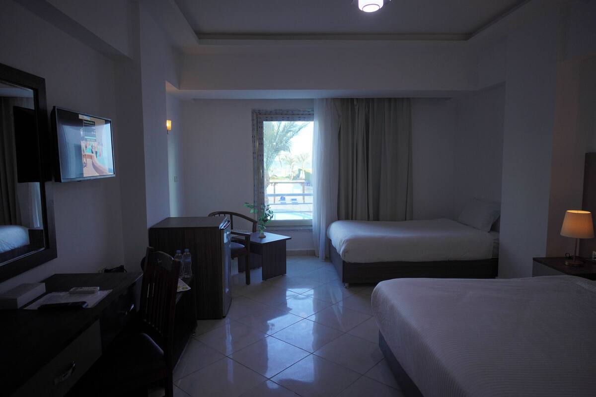 A hotel room with a bed, desk, chair, TV, and a window with curtains.