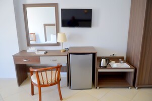 A hotel room with a wooden desk, a chair, a small refrigerator, a television, and a tray with a kettle and cups.