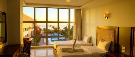A hotel room with two beds, a desk, and a view of a pool and palm trees.