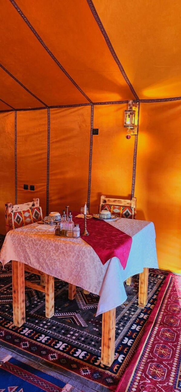 Una habitación con carpa, una cama, una mesa con mantel rojo y una alfombra estampada.