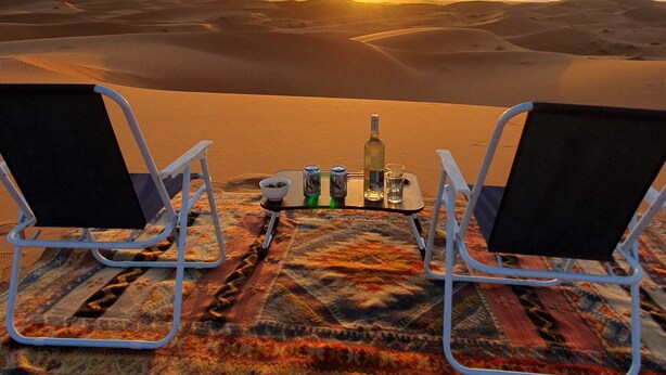 Twee lounge stoelen gericht op een zonsondergang boven een woestijnlandschap.