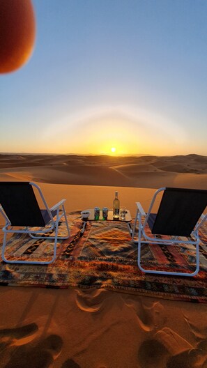Dos sillones de estar mirando una puesta de sol sobre un paisaje desértico.