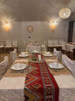 Una larga mesa de comedor con manteles blancos, un camino de mesa estampado y sillas blancas.
