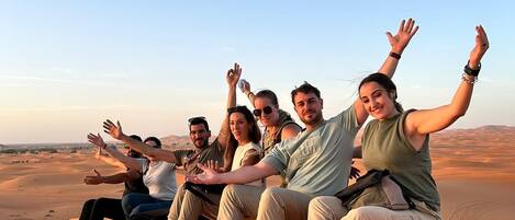 A group of people sitting on a sand dune with a clear sky in the background.