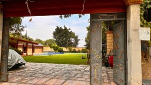 Ein überdachter Patio-Bereich mit einem gepflasterten Weg, der zu einem Pool führt, umgeben von Grünflächen und einem Gebäude mit rotem Dach.