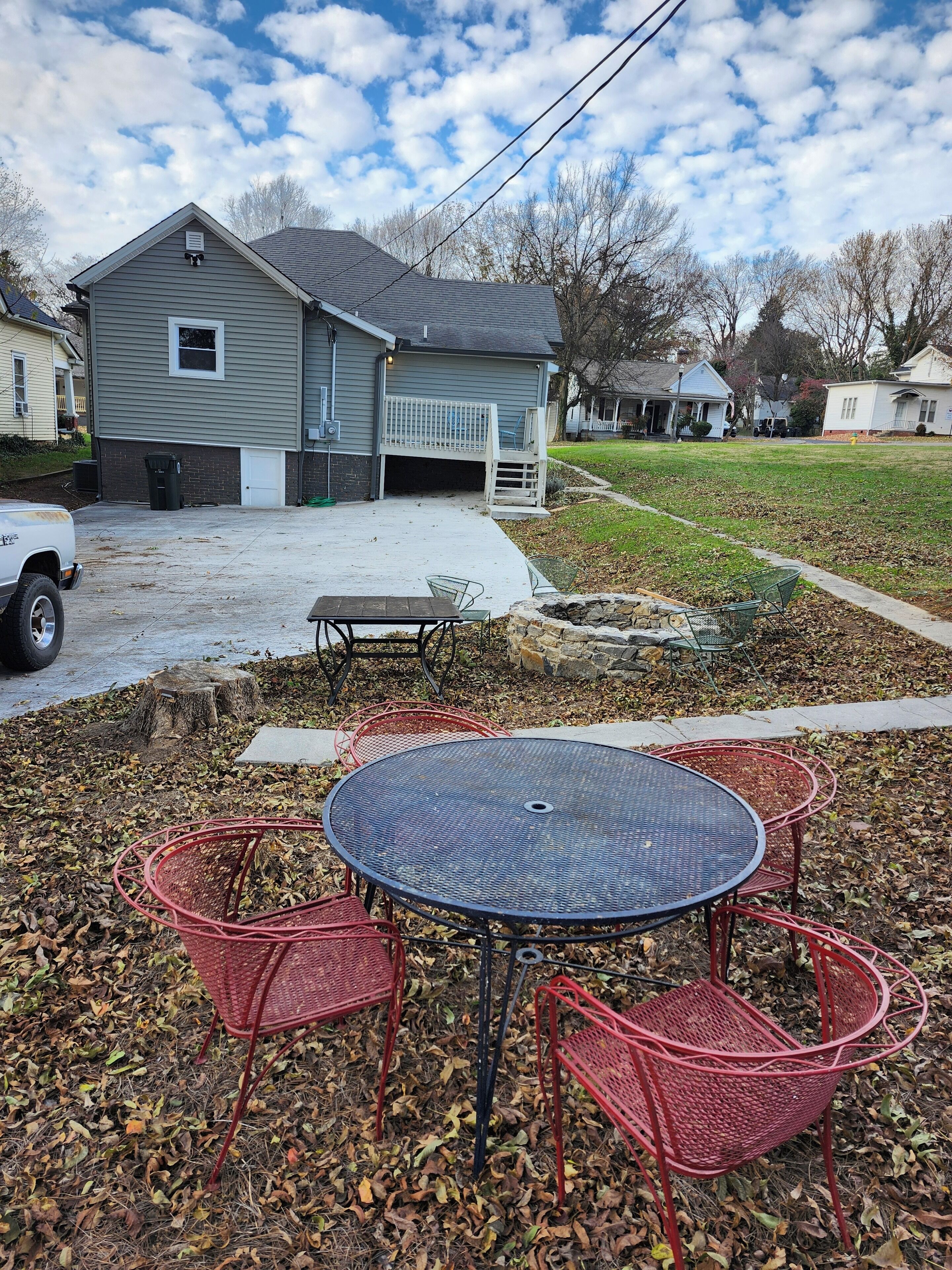 A residential area with a house, a driveway, and a patio with a round table and chairs.