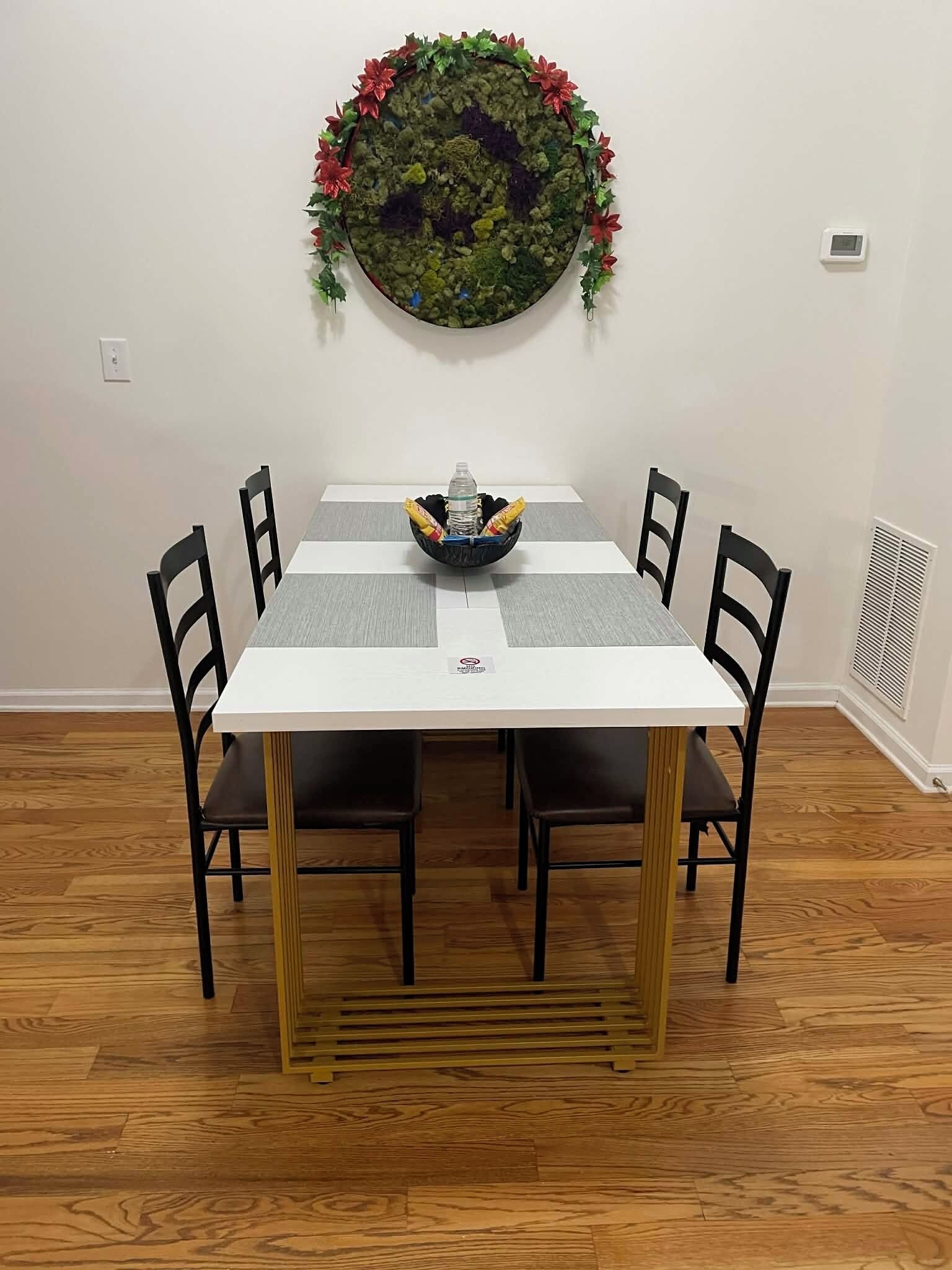 A dining table with four chairs, a bowl with snacks, and a decorative wall hanging above.