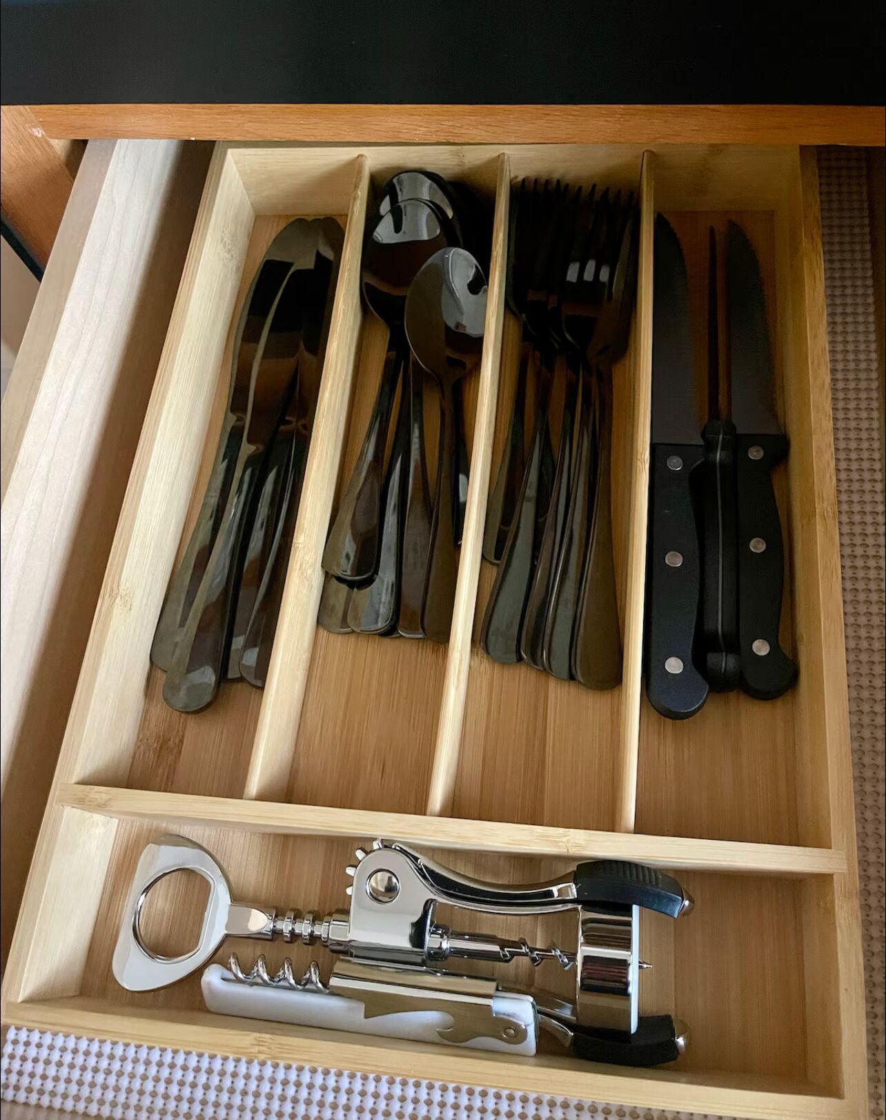 Un tiroir contenant des ustensiles de cuisine bien rangés, notamment des couteaux, des fourchettes et un ouvre-boîte.