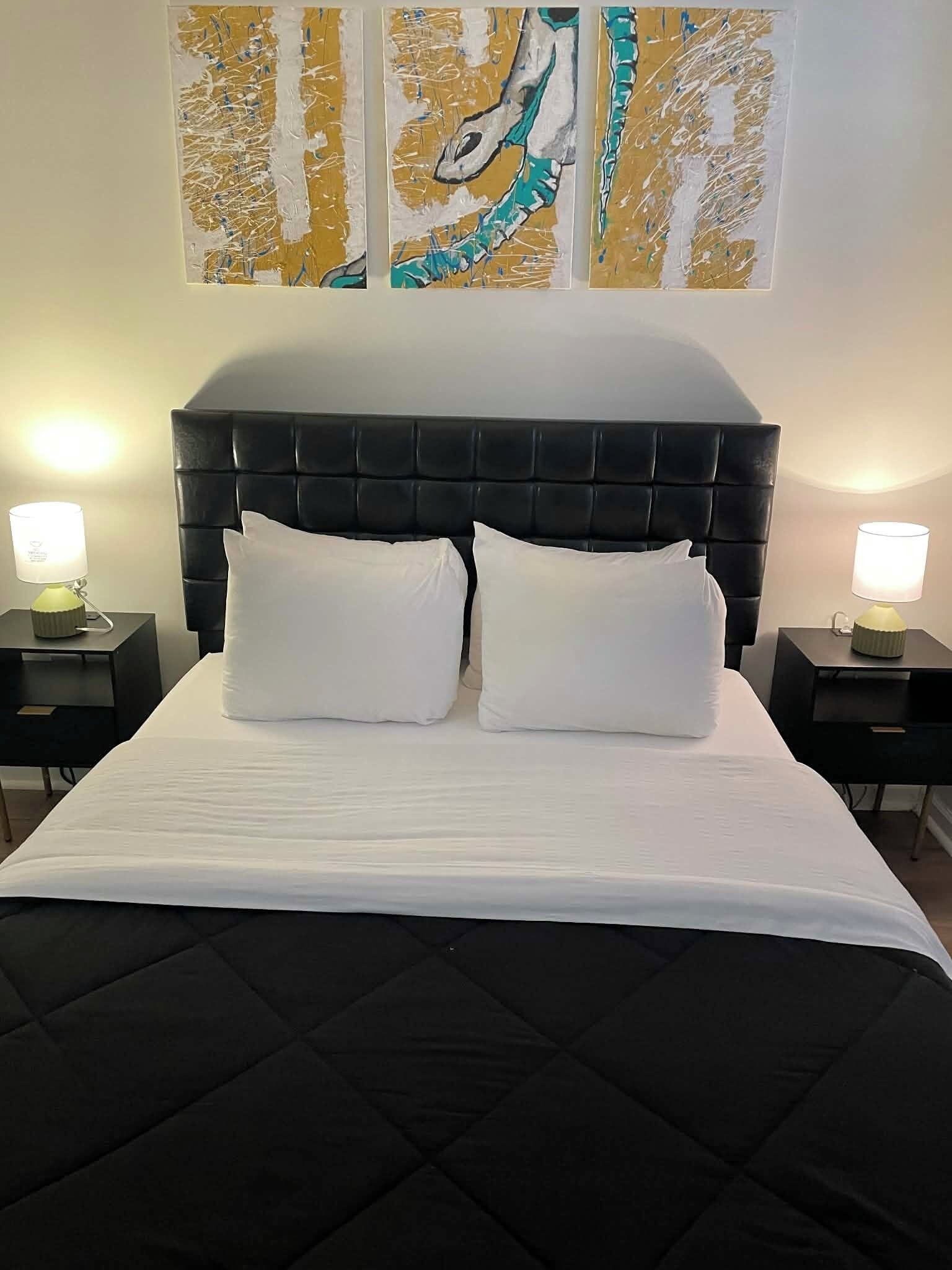 A neatly made bed with a black headboard, two white pillows, and a white bedspread. There are two bedside tables with lamps on either side of the bed.