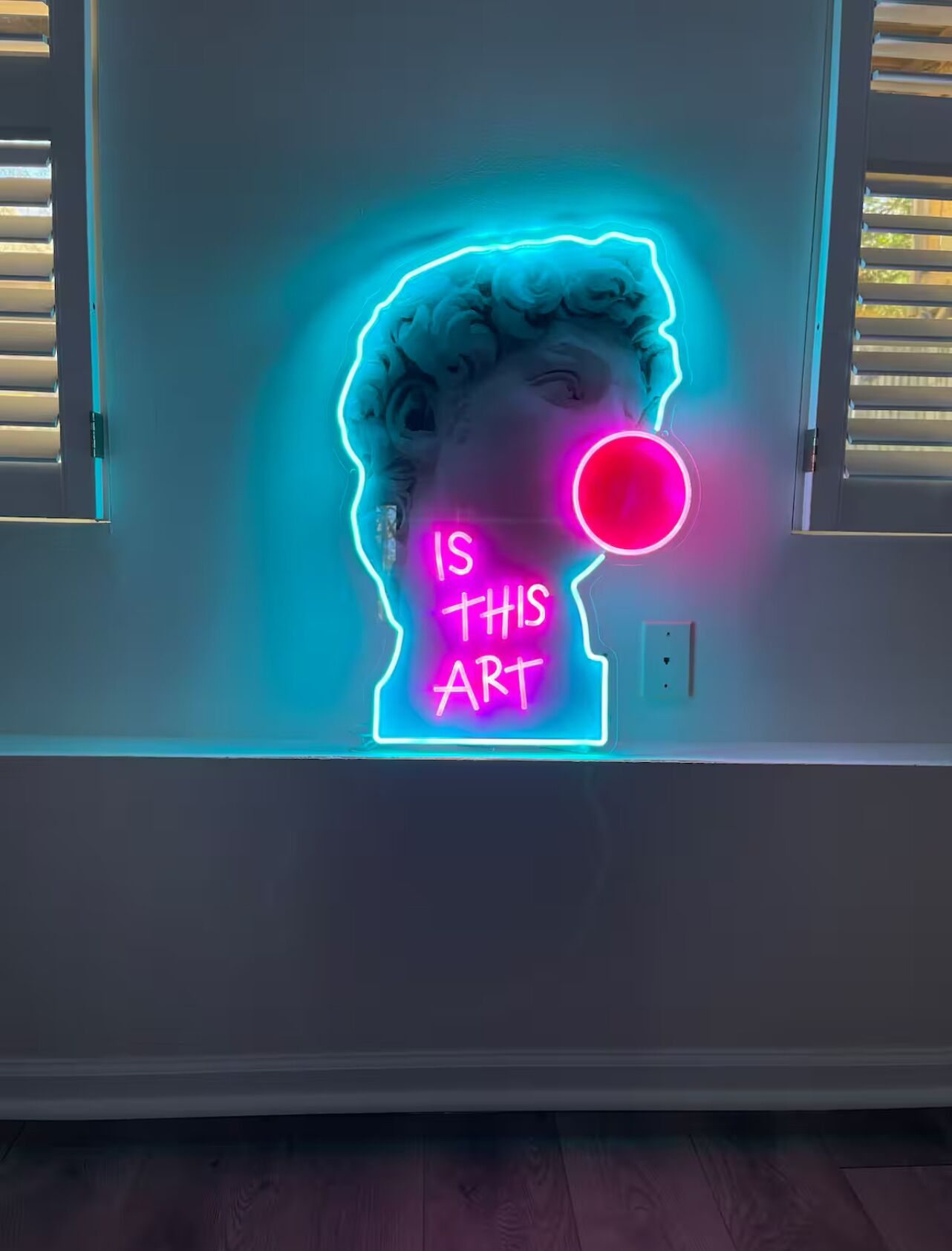 Un letrero de neón con el texto 'IS THIS ART' en una silueta estilizada de una cabeza humana.