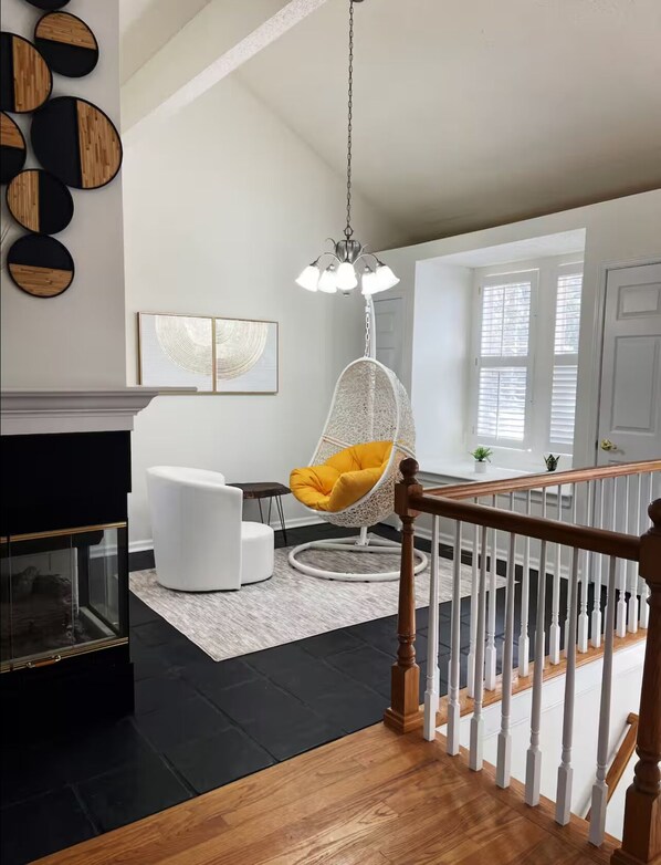 A modern living room with a white sofa, a hanging chair with a yellow cushion, a glass coffee table, and a fireplace.
