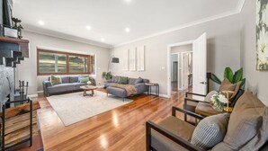A spacious living room with hardwood flooring, a grey sofa, a coffee table, and a large window offering a view of the outdoors.