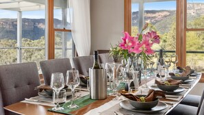 A dining table set for a meal with wine glasses, a bottle, and a vase with flowers.