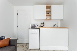 A compact kitchen with white cabinetry, a microwave, a coffee maker, and a small refrigerator.