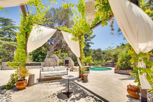 An outdoor patio with a bed, lounge chairs, a pool, and potted plants.