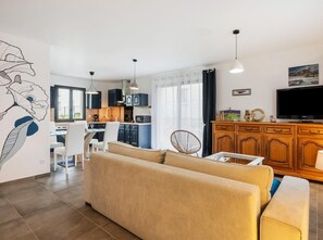 Ein modernes Wohnzimmer mit Sofa, Essbereich, Küche und Fernseher.