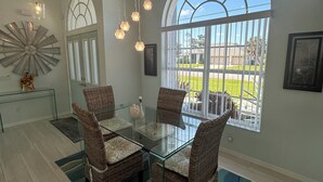 A dining area with a glass table surrounded by wicker chairs, a large arched window, and hanging pendant lights.