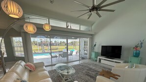 A modern living room with a white leather sofa, a glass coffee table, and a television on a white stand.