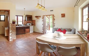 Une cuisine avec un mur en briques, un coin repas avec une table ronde et des chaises, et une vue sur l’extérieur.