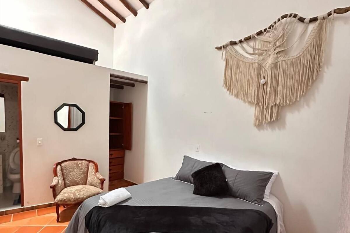 Ein Schlafzimmer mit Bett, Stuhl, Spiegel und einer Wanddeko aus Makramee.