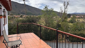 Een terras met een stoel, een rode balustrade en uitzicht op een bergachtig landschap met huizen in de verte.
