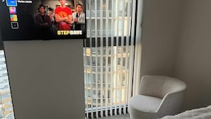 A hotel room with a large window, a white armchair, and a bed with a white blanket. - Luxury Apartment with City Views in the Heart of Bondi Junction (Bondi Junction)