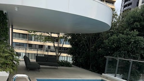 A swimming pool with a metal ladder, a covered seating area, and a view of a modern building with balconies. - Luxury Apartment with City Views in the Heart of Bondi Junction (Bondi Junction)
