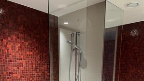 A modern bathroom with a glass-enclosed shower, a white toilet, and a red-tiled wall. - Luxury Apartment with City Views in the Heart of Bondi Junction (Bondi Junction)