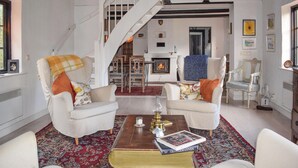 A living room with two white armchairs, a coffee table with books, a fireplace, and a staircase. - Beautiful home in Hammenhög (Hammenhög)