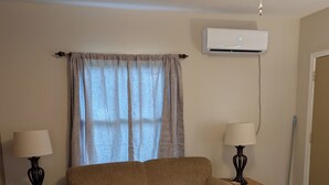 A living room with a sofa, two side tables with lamps, a wooden coffee table, a ceiling fan, and an air conditioning unit. - Charming updated 1-bedroom apartment in brilliant Midland with AC (Midland)