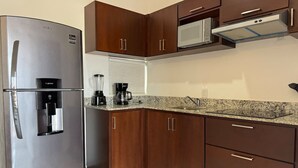 A compact kitchen with a stainless steel refrigerator, a built-in microwave, and wooden cabinets.