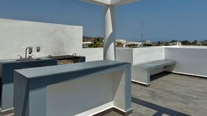 A rooftop terrace with a minimalist design, featuring a built-in sink and a seating area.