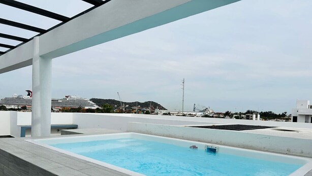 A rooftop swimming pool with a view of a cruise ship and distant buildings.