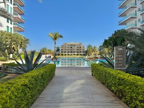 Un resort con piscina centrale, circondato da vegetazione curata e palme.