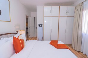Une chambre d’hôtel avec un lit, des rideaux blancs, une armoire et une lampe.