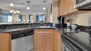 A modern kitchen with a dishwasher, stove, and microwave. It features wooden cabinets, a granite countertop, and pendant lighting.