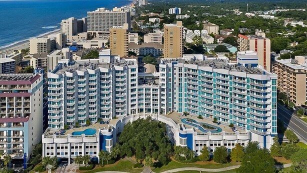 A high-rise hotel with multiple balconies, a swimming pool, and a view of the ocean.