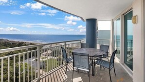 A balcony with a table and chairs, overlooking a coastal view.