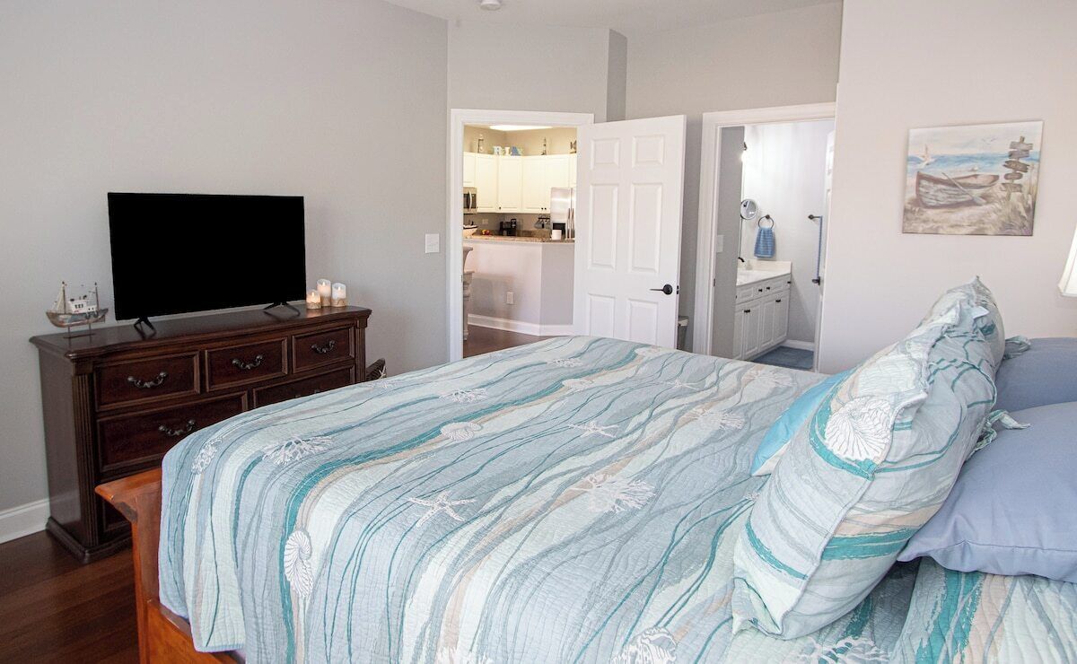 Une chambre à coucher comprenant un lit, une télévision, une commode et une porte donnant sur une salle de bain.